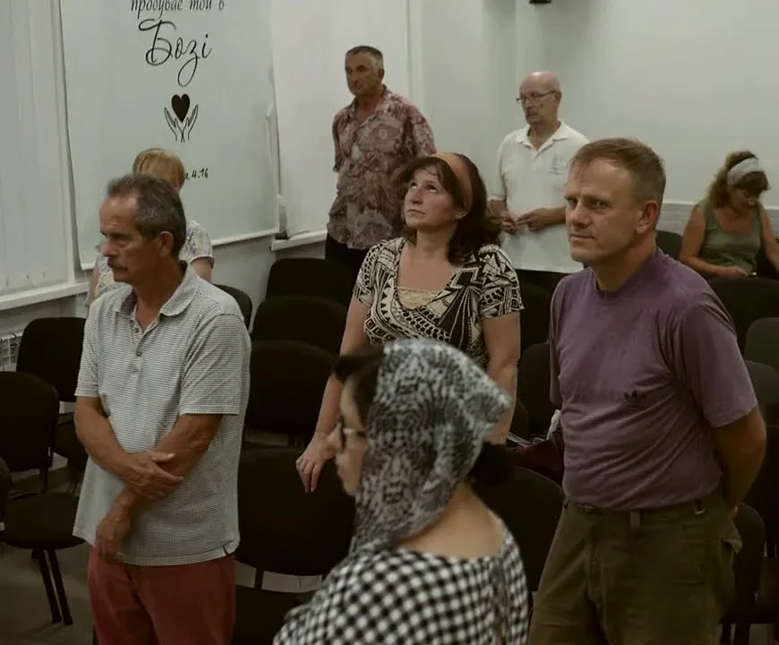 Члени громади стоять між рядами крісел і співають